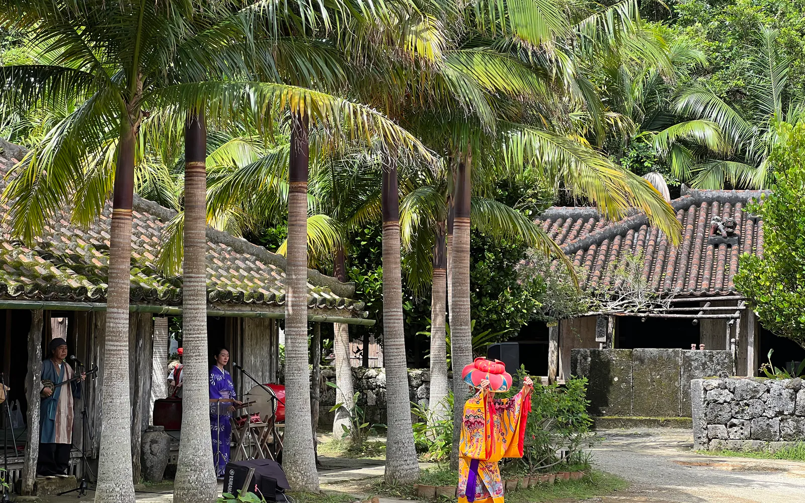 A traditional Okinawan performance among red-tile village homes and palms